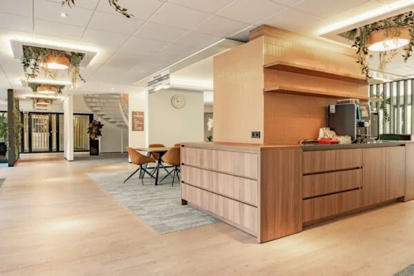 Moderne, lichte ontvangstruimte in het gebouw aan de Burgemeester Verderlaan met zithoek, koffiemeubel en een trap naar boven.